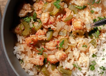 Bowl of steaming étouffée with shrimp and crawfish over white rice, garnished with green onions