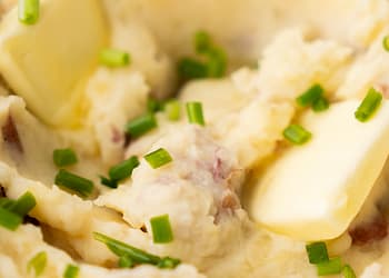 Creamy garlic mashed potatoes in a white bowl with a pat of melting butter and sprinkled with chopped chives