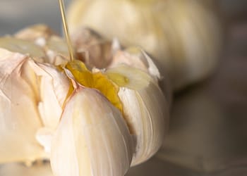 Whole garlic bulb with olive oil being drizzled on top, ready to be roasted for garlic mashed potatoes