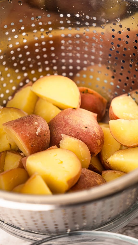 Cut red potatoes draining in a colander after boiling, ready for making garlic mashed potatoes