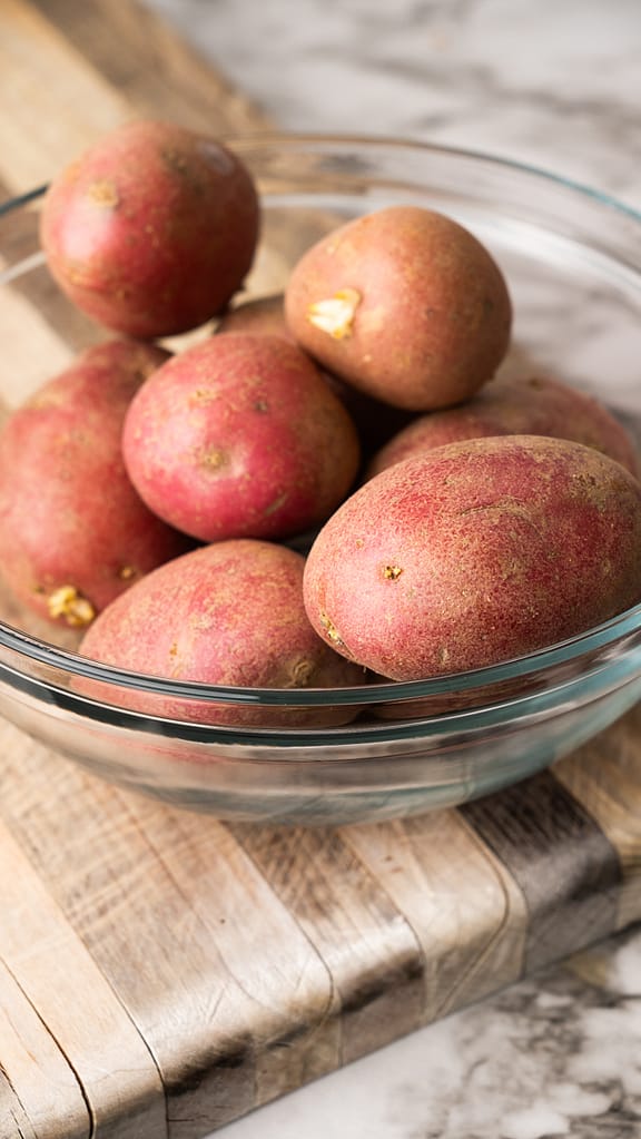 Fresh red potatoes being prepared for garlic mashed potatoes recipe, showing whole and cut potatoes with skins on