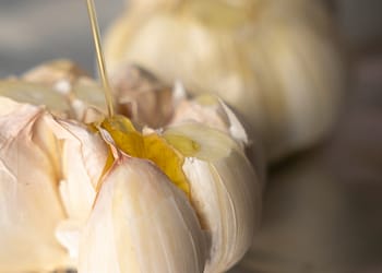 Whole garlic bulb with olive oil being drizzled on top, ready to be roasted for garlic mashed potatoes