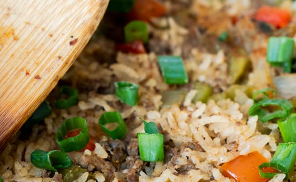 Cajun Dirty Rice in a cast iron skillet with a wooden spoon