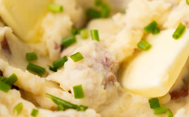 Creamy garlic mashed potatoes in a white bowl with a pat of melting butter and sprinkled with chopped chives