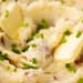 Creamy garlic mashed potatoes in a white bowl with a pat of melting butter and sprinkled with chopped chives