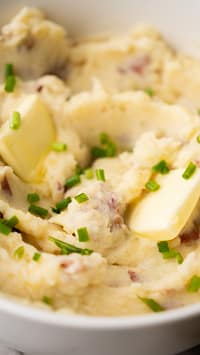 Creamy garlic mashed potatoes in a white bowl with a pat of melting butter and sprinkled with chopped chives