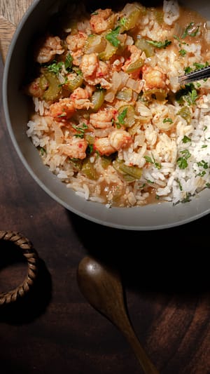 Bowl of steaming étouffée with shrimp and crawfish over white rice, garnished with green onions
