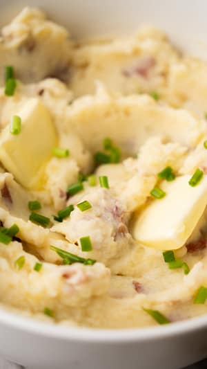 Creamy garlic mashed potatoes in a white bowl with a pat of melting butter and sprinkled with chopped chives