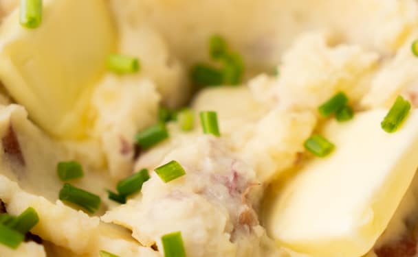 Creamy garlic mashed potatoes in a white bowl with a pat of melting butter and sprinkled with chopped chives