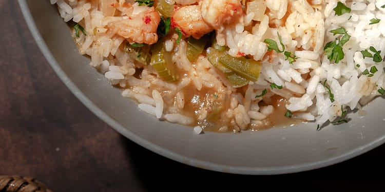 Bowl of steaming étouffée with shrimp and crawfish over white rice, garnished with green onions