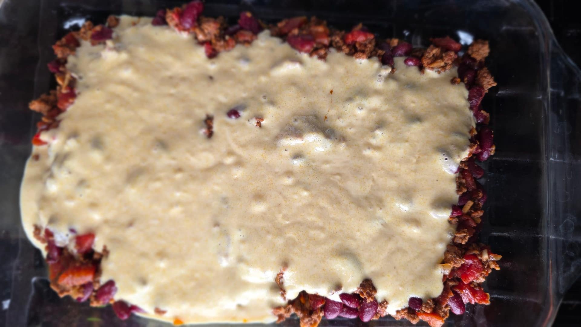 Cornbread batter poured over chili in casserole dish